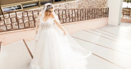 Bride wearing Harlem off-the-shoulder wedding dress by Maggie Sottero on the steps of her venue.