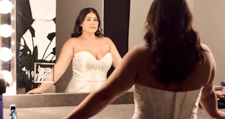 Bride wearing Missy plus size wedding dress by Rebecca Ingram looking at herself in the mirror.