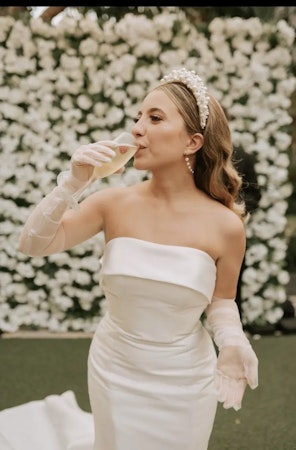 Bride wearing Mitchell satin wedding dress by Maggie Sottero and sipping champagne.