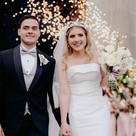 Bride wearing Mitchell simple wedding dress by Maggie Sottero holding hands with her husband.