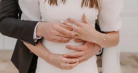 Bride wearing Kashlynn wedding dress with sleeves by Maggie Sottero exchanging rings with her husband.