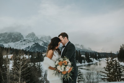 Winifred bride in snowy mountains holding bouquet with groom
